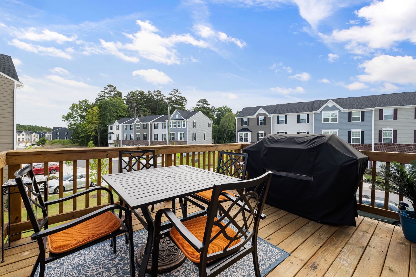 A wooden backyard deck furnished with a table, chairs and a grill