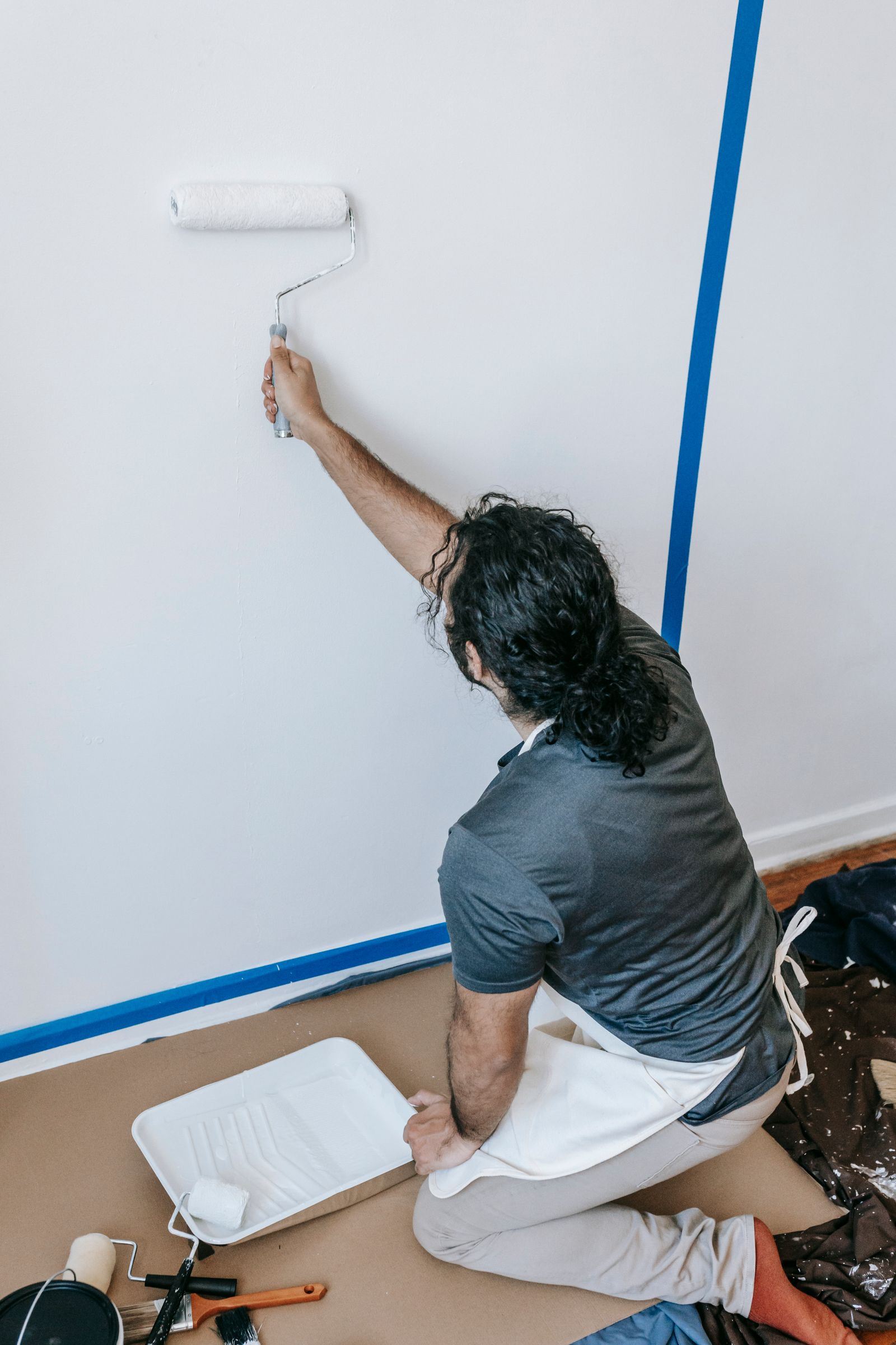 A handyman rolling fresh white paint onto an interior wall beside taped trim
